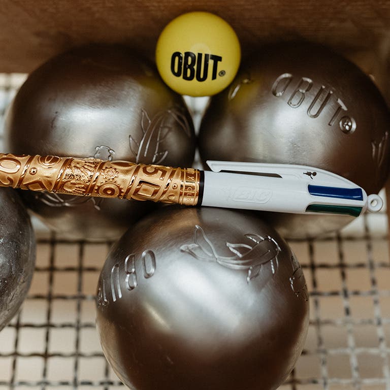 Stylo BIC 4 Couleurs Obut x Tournaire rose posé sur des boules de pétanque avec un cochonnet Obut