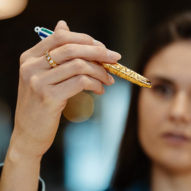 Femme tenant le stylo BIC 4 Couleurs Obut x Tournaire version or avec une bague Tournaire